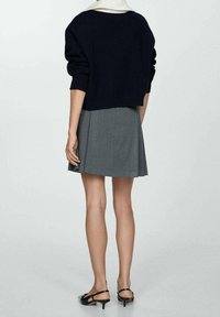 Suéter recortado azul marino con mangas voluminosas, combinado con una falda mini plisada gris. Tacones negros con tiras completan el conjunto.