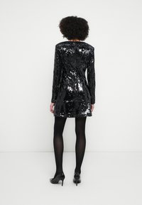 Melna spīdīga kleita ar garām piedurknēm, apaļu kakla izgriezumu, piegulošu siluetu un izplestiem svārkiem, kombinēta ar melniem augstpapēžu kurpēm un caurspīdīgām zeķubiksēm.