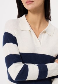Maglione leggero con righe orizzontali blu navy e crema, colletto e polsini a coste per un tocco di consistenza.