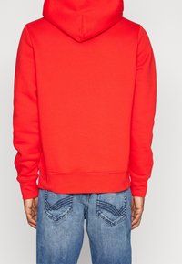 Rode pullover hoodie met een kangoeroezak, ribbelmanchetten en -zoom. Gepaard met blauwe denim jeans met gebogen achterzakontwerpen.