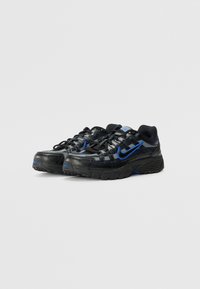 Baskets Nike noires et bleues avec une tige en mesh et cuir, une semelle en caoutchouc épaisse, et un logo swoosh bleu bien en vue.