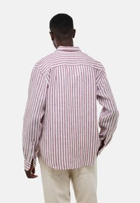 Chemise à manches longues rayée en lin rouge et blanc, poignets boutonnés, ourlet arrondi, couture de bas de dos, texture visible due au tissage du tissu.