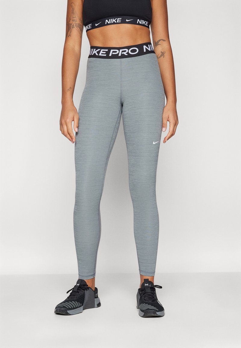 Legginsy Nike Pro w kolorze heather gray, dopasowane z płaskimi szwami. Zawierają czarny pas z powtarzającym się tekstem "Nike Pro" i małym logo.