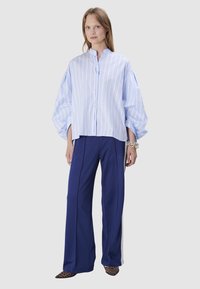 Light blue and white striped button-up shirt with puffed sleeves, paired with navy blue wide-leg trousers featuring side stripes and leopard print shoes.