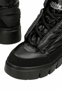 Czarne wysokie trampki z błyszczącą, wyściełaną teksturą, grubą podeszwą i czarnymi sznurówkami. Logo umieszczone na języku oraz pięcie.