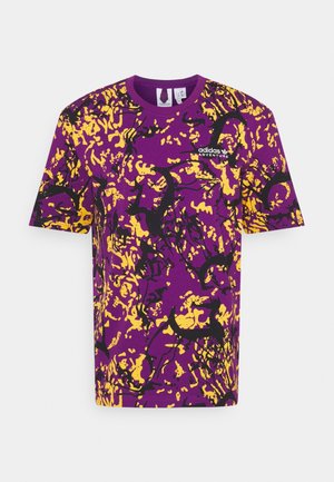 Fioletowa koszulka z abstrakcyjnym żółto-czarnym wzorem rozprysków, dekolt okrągły, krótkie rękawy oraz logo „adidas Adventure” na przodzie.