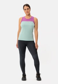 Canottiera verde menta con dettagli viola, realizzata in tessuto leggero. Abbinata a leggins neri con pannelli testurizzati e scarponi da trekking.