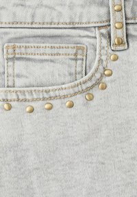 Poche en denim gris clair avec coutures orange et rivets en laiton soulignant la poche et la zone des passants de ceinture.