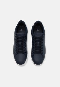 Pár tmavomodrých nízkých tenisek s černými tkaničkami a bílými podrážkami, z pohledu shora na bílém pozadí.