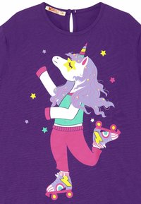 Paarse t-shirt met een eenhoornafbeelding met roze en groene accenten, rolschaatsen en sterdetails, ontworpen in gedurfde, heldere kleuren.