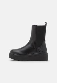 Bottes chelsea en cuir noir avec panneaux élastiques sur les côtés, accents à motif crocodile texturé, semelle épaisse et languette de traction.