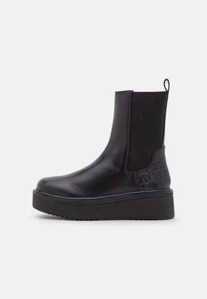 Black leather ankle boots with elastic side panels, textured crocodile pattern accents, chunky platform sole, and pull tab.