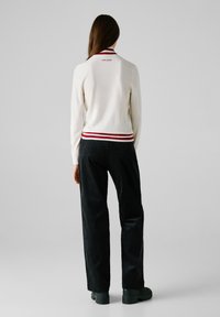 Maglione bianco a maglia con colletto a righe rosse e bianche, abbinato a pantaloni in corduroy neri e scarpe con plateau verde scuro.