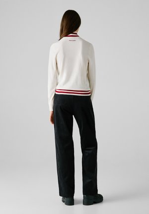 Maglione bianco a maglia con colletto a righe rosse e bianche, abbinato a pantaloni in corduroy neri e scarpe con plateau verde scuro.