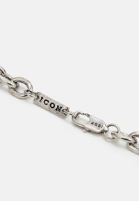 Pulseira de corrente prateada com elos texturizados, uma placa retangular gravada com "ICON" e um fecho seguro.