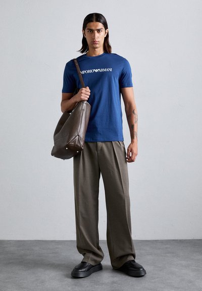 Tricou din bumbac bleu închis cu logo-ul "Emporio Armani", pantaloni largi bej și geantă de umăr din piele maro cu finisaj texturat și accente metalice.