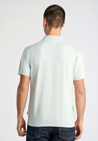 Vaaleansininen lyhythihainen polo-paita, jossa on ribbykaulus ja -helma, teksturoitu kangas ja sivuhalkiot. Yhdistetty tummansinisiin farkkuihin.