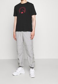 Czarny T-shirt z czerwoną grafiką, zestawiony z jasnoszarymi spodniami cargo i białymi, masywnymi sneakersami. Gładka faktura, swobodny krój.