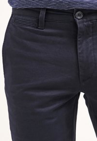 Námorně modré bavlněné chinos kalhoty s hladkou texturou, předním zapínáním na knoflík a decentním designem zadní kapsy. Přiléhavý střih a čisté linie.