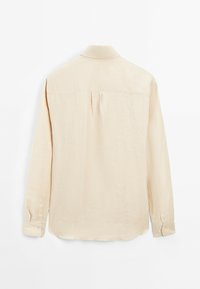Camicia beige a maniche lunghe in tessuto leggero con colletto classico. Presenta una piega sul retro e polsini con bottone, con un orlo dritto.
