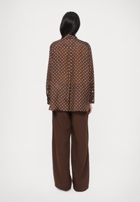 Bluza maro cu buline, croială lejeră; mâneci lungi și guler ascuțit. Asortată cu pantaloni maro, cu picioare largi și uni.