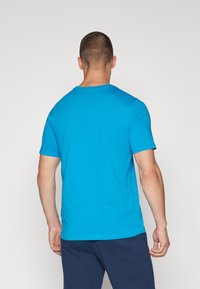 Camiseta de algodón azul con mangas cortas y escote redondo. Textura suave sin patrones o gráficos visibles. Se muestra la vista posterior.