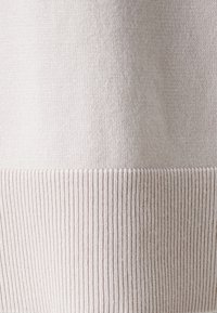 Jasno beżowa dzianina z prążkowaną strukturą na dole. Cała powierzchnia jest gładka, prezentując jednolity kolor bez wzorów.