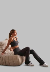Reggiseno sportivo a coste nere e leggings abbinati indossati mentre si è seduti su una poltrona curva e testurizzata beige, con uno sfondo chiaro.