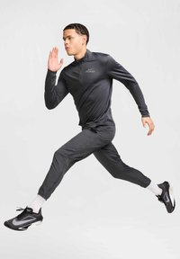 Tummanharmaa urheiluasu, jossa on neljänneksen vetoketjulla varustettu paita ja kapenevat housut. Varustettu heijastavalla logolla ja tyylikkäillä mustilla lenkkitossuilla. Sileä, kevyt materiaali.