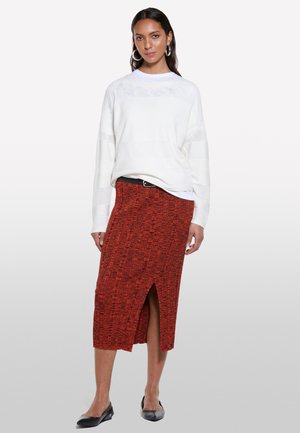 Maglione bianco a trama con maniche lunghe, abbinato a una gonna a tubino rossa con motivo e spacco laterale, e scarpe flat nere.