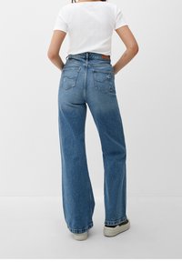 Höga, vida blå jeans i denim med en blekt finish, två bakfickor och en fransad fåll. Parat med vita sneakers.