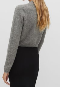 Pull gris raccourci à manches longues, fabriqué en maille douce. Comprend des poignets et un ourlet côtelés, porté sur une jupe noire.