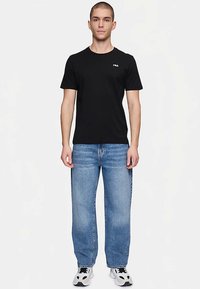 Svart bomulls-T-shirt med rund hals och korta ärmar, med en liten röd och vit logotyp på bröstet. Kombinerad med ljusblå jeans.