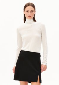 Witte lange mouw turtleneck top gecombineerd met een zwarte minirok met een zijopening. Glad materiaal, aangesloten ontwerp en strakke lijnen.