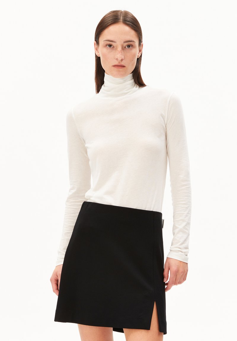 Witte lange mouw turtleneck top gecombineerd met een zwarte minirok met een zijopening. Glad materiaal, aangesloten ontwerp en strakke lijnen.
