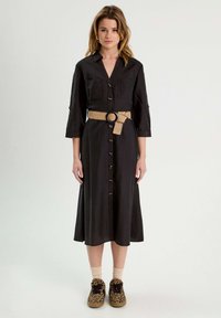Robe noire à manches trois-quarts, dotée d'une ceinture à la taille en matériau tissé tan, associée à des chaussures et des chaussettes à imprimé léopard.