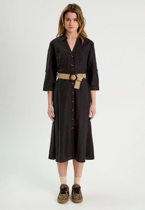 Robe noire à manches trois-quarts, dotée d'une ceinture à la taille en matériau tissé tan, associée à des chaussures et des chaussettes à imprimé léopard.