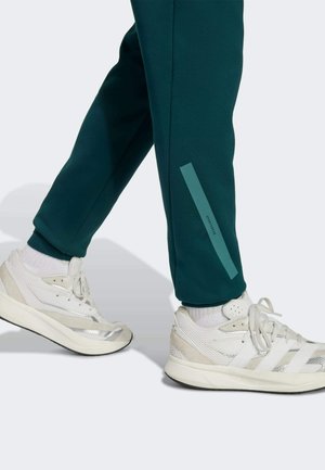 Dark teal jogger pants with a slim fit feature a side accent stripe. Paired with white athletic shoes with silver details and laces.