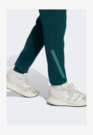 Mørk teal joggerbukser med en slim fit har en sideløsningstribe. Sammen med hvide atletiske sko med sølvdetaljer og snørebånd.