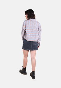 Veste à manches longues, cropped, à motifs avec des designs bleu, rose et blanc, associée à une jupe en denim foncé et des bottes noires à lacets.