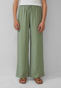 Hellgrüne, weit geschnittene Hosen aus strukturiertem Stoff, mit elastischem Bund und Kordelzug, kombiniert mit braunen, schnürbaren Sandalen.