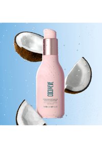 Rosa flaska med leave-in balsam och metalllock, omgiven av kokoshälftar och vattendroppar mot en blå bakgrund.