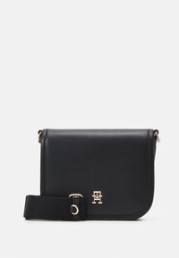 Borsa a tracolla in pelle nera con logo dorato, forma rettangolare e tracolla in tessuto. Texture liscia con bordi angolari e dettagli in metallo dorato.
