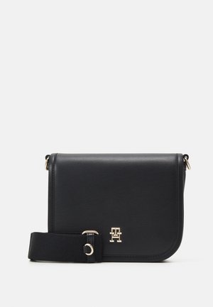 Borsa a tracolla in pelle nera con logo dorato, forma rettangolare e tracolla in tessuto. Texture liscia con bordi angolari e dettagli in metallo dorato.