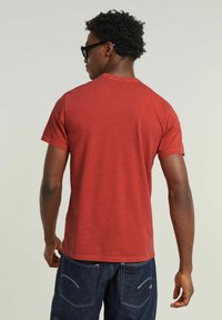 T-shirt rossa in cotone con scollo rotondo e maniche corte, caratterizzata da una texture liscia. Indossata con pantaloni di jeans scuri e una vestibilità casual.