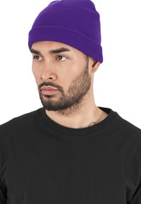 Beanie viola a maglia con una texture a coste, orlo piegato, indossato da una persona con una maglietta nera. Design semplice e aderente.
