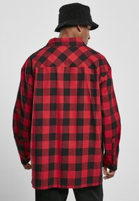 Rød og sort ternet flannel skjorte med afslappet pasform, lange ærmer og knaplukning ved manchetterne. Mønsteret har store firkanter.