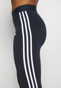 Navy leggings with three white stripes down the side, designed with a high waistband and made from a smooth, stretchy fabric.