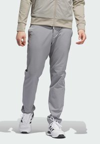Pantalons de sport gris clair avec une coupe fuselée, texture lisse, poches latérales et taille élastique, associés à des baskets blanches.