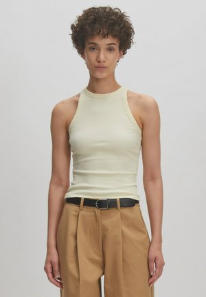 Rippentop ohne Ärmel in Cremefarbe mit hochgeschlossenem Hals. Kombiniert mit lockeren, beigen Hosen und einem schwarzen Gürtel. Glatte Textur und figurbetonte Silhouette.